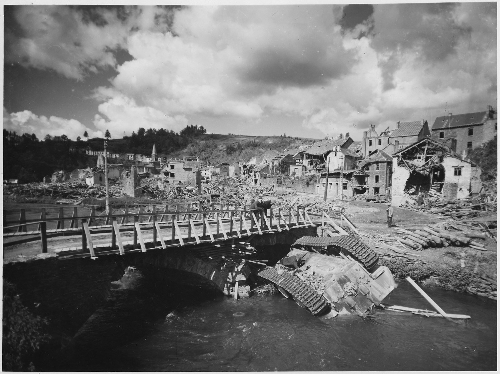 An overturned German tank lies in a shallow stream alongside a rebuilt bridge in war-ravaged Houffalizo, Belgium.